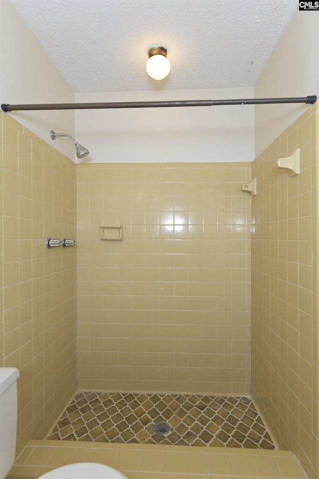 bathroom with a tile shower, toilet, and a textured ceiling