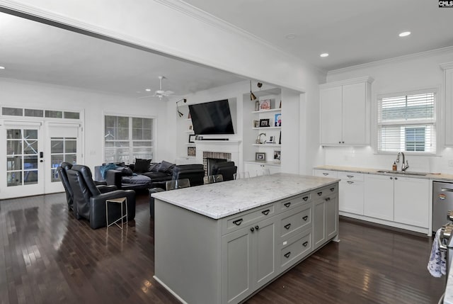 kitchen featuring sink, white cabinetry, a center island, a brick fireplace, and light stone countertops