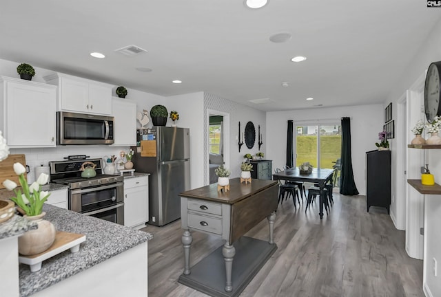 kitchen featuring appliances with stainless steel finishes, white cabinetry, backsplash, light stone counters, and light wood-type flooring