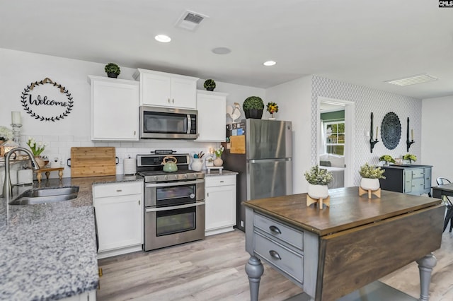 kitchen with tasteful backsplash, sink, dark stone countertops, white cabinets, and stainless steel appliances