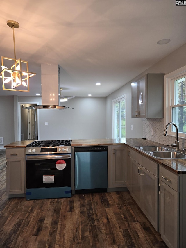 kitchen with appliances with stainless steel finishes, island range hood, decorative light fixtures, sink, and kitchen peninsula