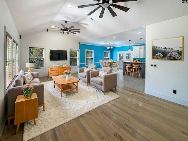 living room with hardwood / wood-style floors, ceiling fan with notable chandelier, and vaulted ceiling