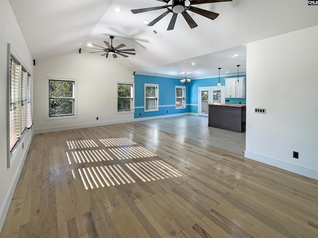 unfurnished living room with hardwood / wood-style flooring, vaulted ceiling, and ceiling fan with notable chandelier