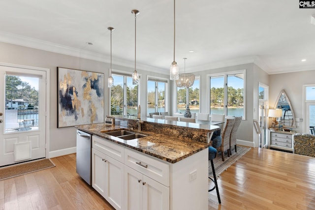 kitchen featuring white cabinetry, dark stone countertops, a water view, a center island with sink, and decorative light fixtures