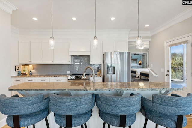 kitchen featuring hanging light fixtures, an island with sink, white cabinets, stainless steel fridge with ice dispenser, and custom exhaust hood