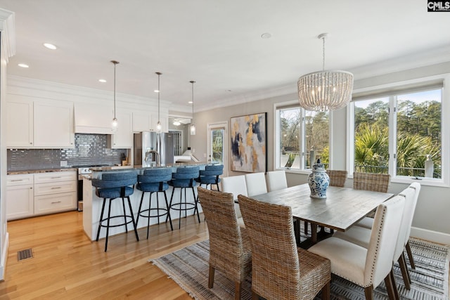 dining space with an inviting chandelier, ornamental molding, plenty of natural light, and light hardwood / wood-style floors