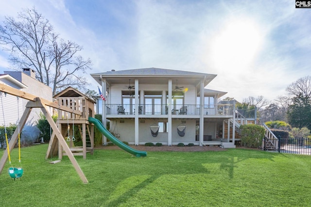 rear view of house with ceiling fan, a playground, and a lawn