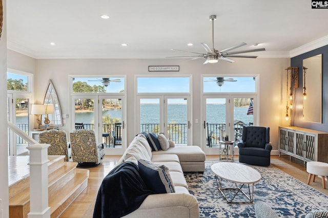 living room featuring light hardwood / wood-style flooring, crown molding, a wealth of natural light, and a water view