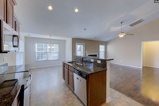 kitchen with lofted ceiling, sink, stainless steel appliances, decorative light fixtures, and dark stone counters