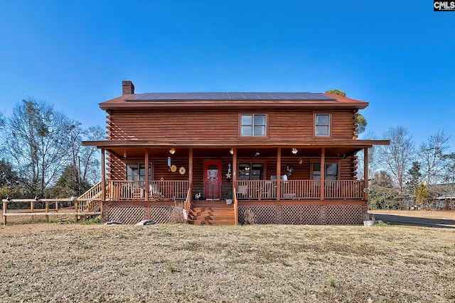 log home featuring covered porch, a front yard, and solar panels