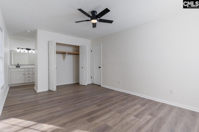 unfurnished bedroom featuring sink, ensuite bath, a textured ceiling, light wood-type flooring, and ceiling fan