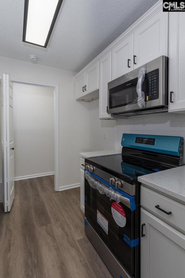 kitchen featuring appliances with stainless steel finishes, white cabinetry, dark hardwood / wood-style flooring, light stone countertops, and a textured ceiling