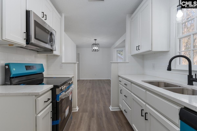 kitchen with sink, appliances with stainless steel finishes, white cabinetry, dark hardwood / wood-style flooring, and decorative light fixtures