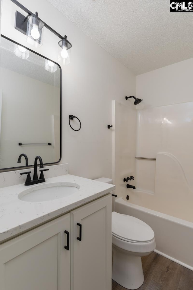 full bathroom featuring toilet, bathing tub / shower combination, wood-type flooring, a textured ceiling, and vanity