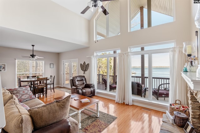 living room featuring a towering ceiling, light wood-type flooring, ceiling fan, and a water view