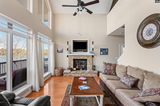 living room with a fireplace, a towering ceiling, light hardwood / wood-style flooring, and ceiling fan