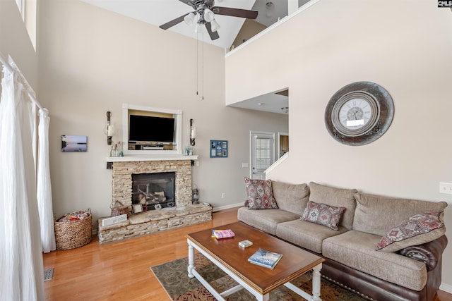 living room with a stone fireplace, wood-type flooring, high vaulted ceiling, and ceiling fan