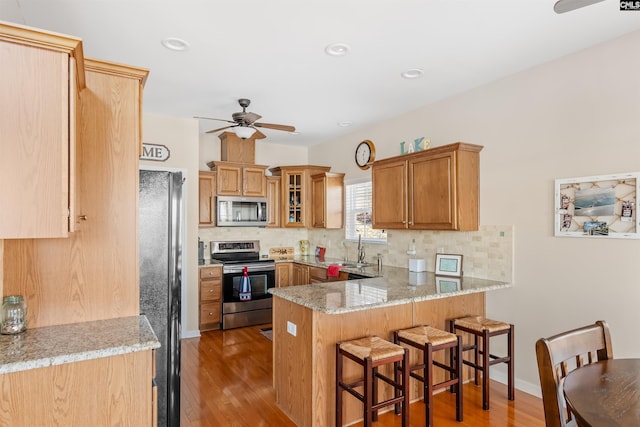 kitchen featuring stainless steel appliances, backsplash, light wood-type flooring, and kitchen peninsula