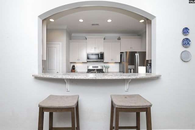 kitchen featuring a breakfast bar, white cabinetry, crown molding, tasteful backsplash, and appliances with stainless steel finishes