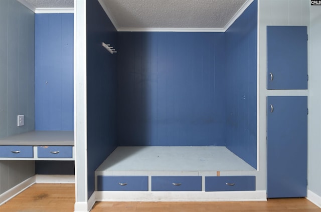 mudroom featuring hardwood / wood-style flooring, wooden walls, ornamental molding, and a textured ceiling