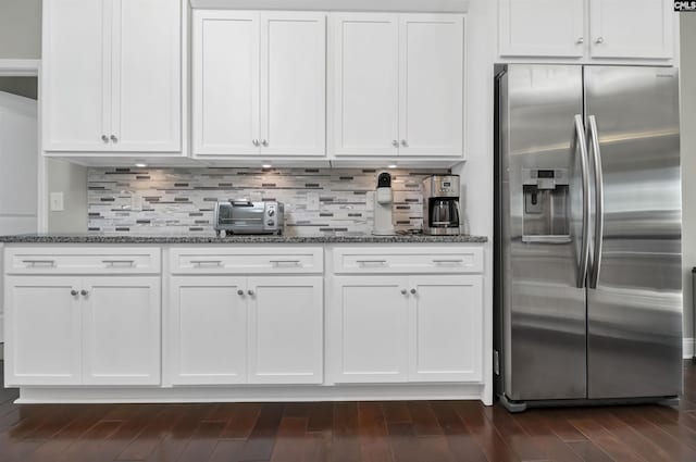 kitchen with stainless steel refrigerator with ice dispenser, white cabinetry, tasteful backsplash, and dark stone countertops