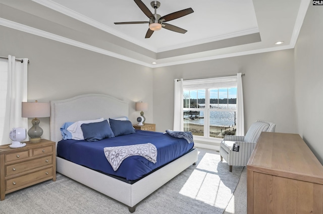 carpeted bedroom with a raised ceiling, crown molding, a water view, and ceiling fan