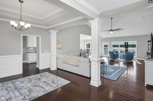 living room with crown molding, ceiling fan with notable chandelier, dark wood-type flooring, and decorative columns