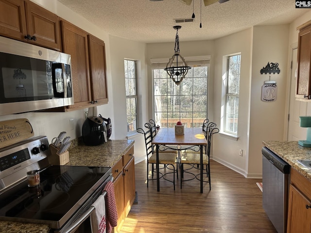 kitchen with pendant lighting, dark wood-type flooring, appliances with stainless steel finishes, light stone countertops, and a textured ceiling