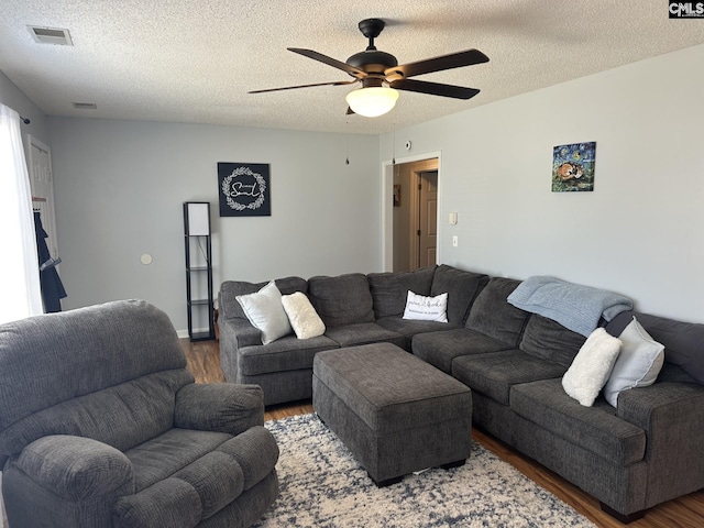 living room featuring dark wood-type flooring, ceiling fan, and a textured ceiling