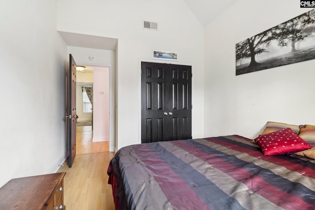 bedroom featuring high vaulted ceiling, light hardwood / wood-style floors, and a closet