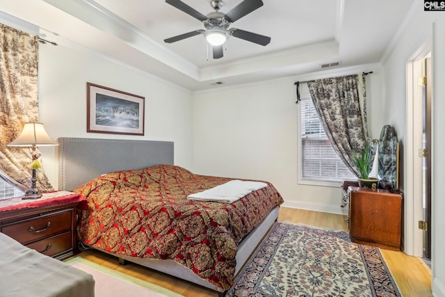 bedroom featuring a raised ceiling, crown molding, light wood-type flooring, and ceiling fan