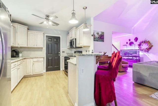 kitchen with appliances with stainless steel finishes, decorative light fixtures, tasteful backsplash, light hardwood / wood-style floors, and light stone counters