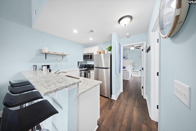 kitchen with a breakfast bar area, white cabinetry, dark hardwood / wood-style floors, kitchen peninsula, and stainless steel appliances