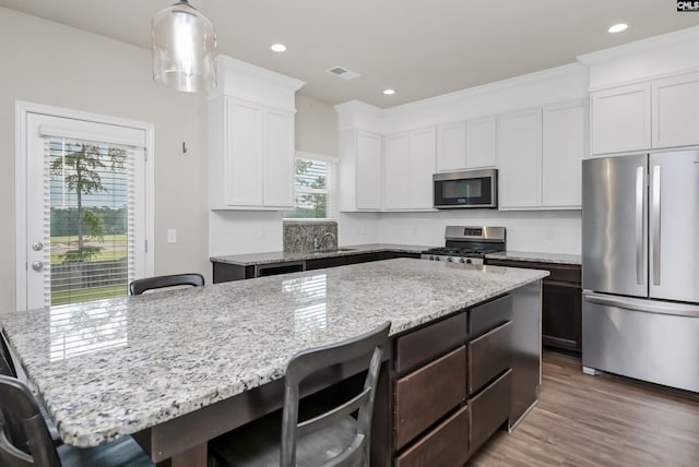 kitchen with a breakfast bar, a center island, hanging light fixtures, appliances with stainless steel finishes, and white cabinets