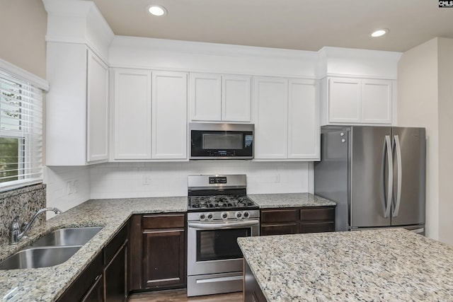 kitchen with appliances with stainless steel finishes, tasteful backsplash, white cabinetry, sink, and dark brown cabinets