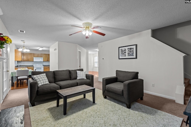 carpeted living room featuring ceiling fan with notable chandelier and a textured ceiling