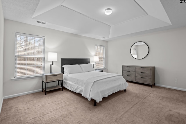 bedroom with multiple windows, light carpet, and a tray ceiling