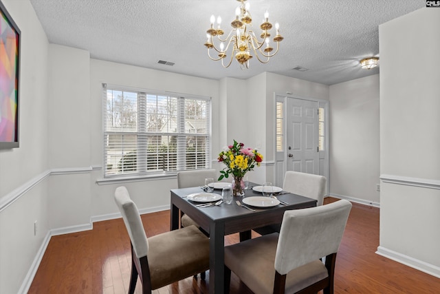 dining area with dark hardwood / wood-style flooring, a textured ceiling, and an inviting chandelier