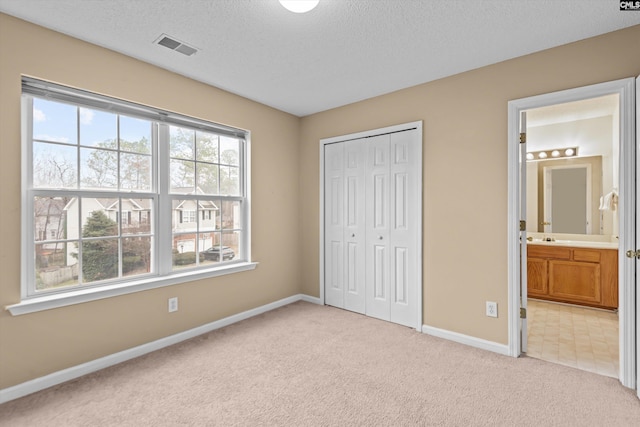 unfurnished bedroom with ensuite bathroom, light carpet, a textured ceiling, and a closet