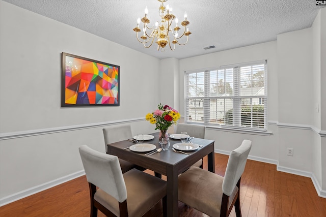 dining room with dark wood-type flooring, a textured ceiling, and a notable chandelier