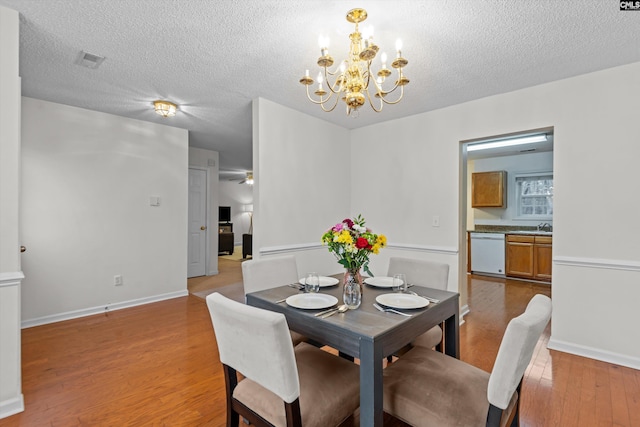 dining space with an inviting chandelier, a textured ceiling, and light wood-type flooring