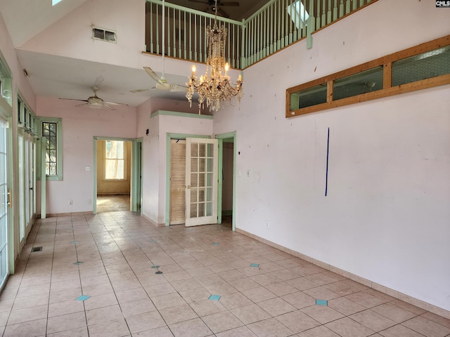 spare room featuring ceiling fan with notable chandelier, light tile patterned floors, and a high ceiling