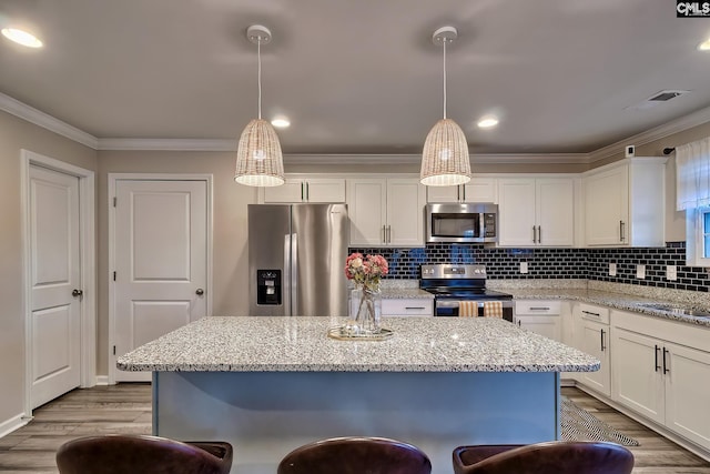 kitchen with pendant lighting, stainless steel appliances, a kitchen island, and white cabinets