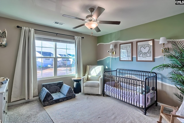 carpeted bedroom with a crib and ceiling fan