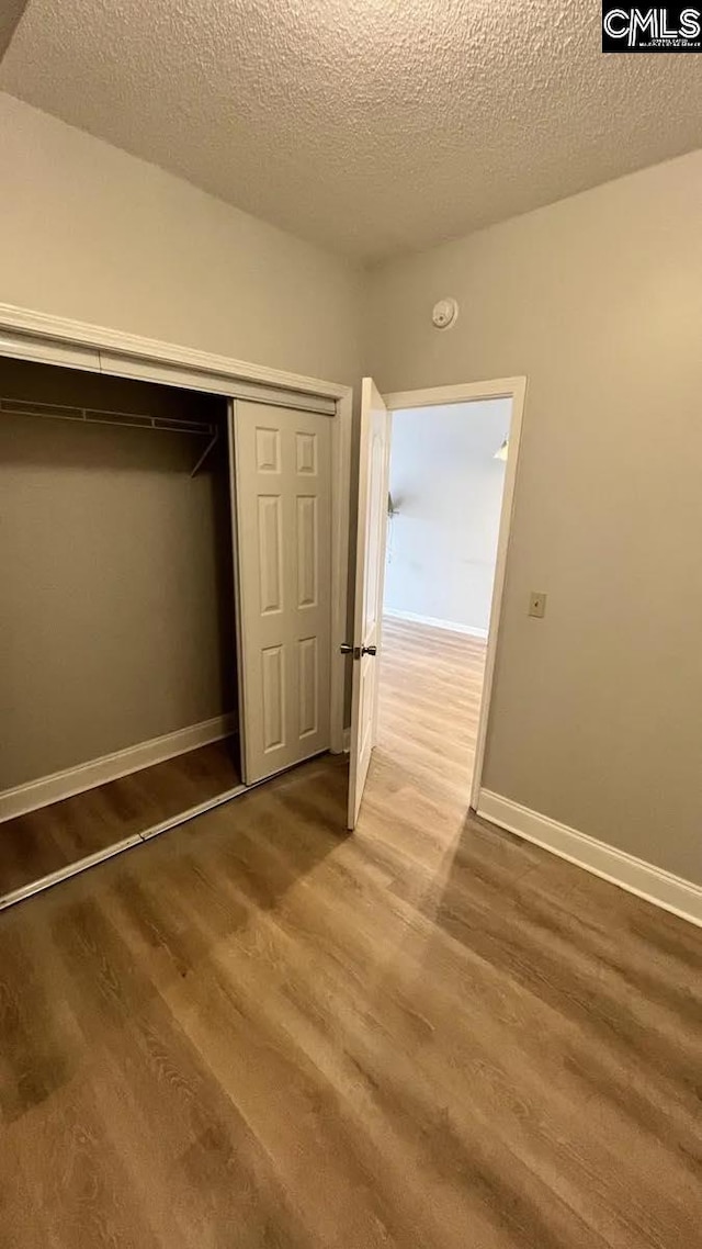 unfurnished bedroom featuring wood-type flooring, a closet, and a textured ceiling