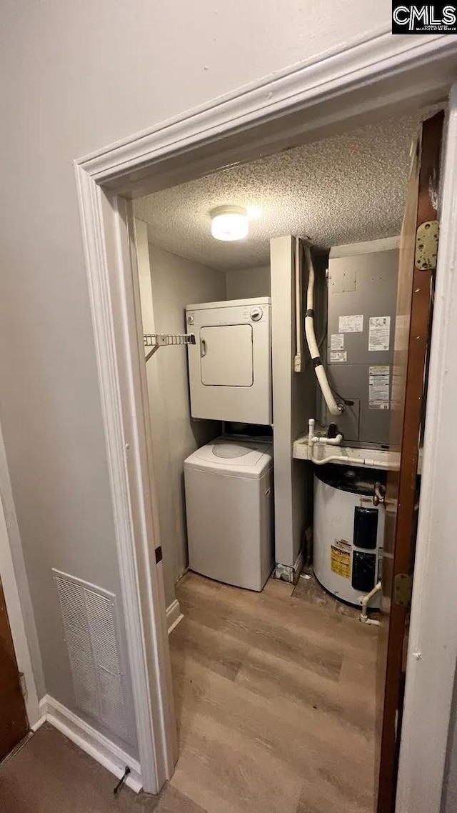 laundry area featuring stacked washer / dryer, wood-type flooring, and a textured ceiling