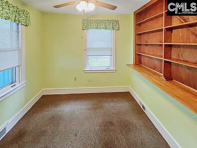 carpeted spare room featuring built in shelves, plenty of natural light, and ceiling fan