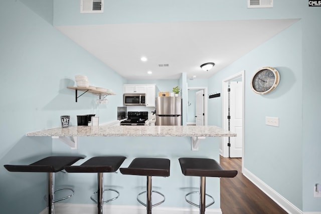 kitchen with dark wood-type flooring, a breakfast bar, kitchen peninsula, stainless steel appliances, and white cabinets