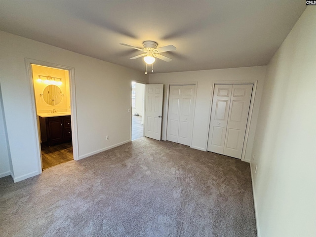 unfurnished bedroom featuring ensuite bathroom, sink, light colored carpet, multiple closets, and ceiling fan