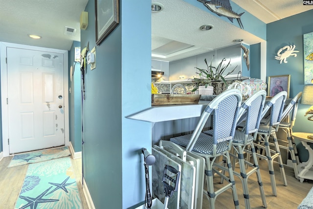 interior space featuring sink, a textured ceiling, light wood-type flooring, and a tray ceiling